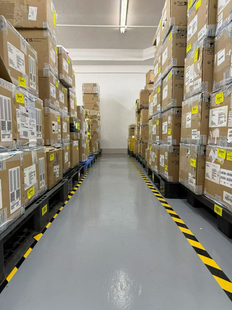 Pasillo de almacén con cajas de cartón etiquetadas apiladas sobre palés a ambos lados
